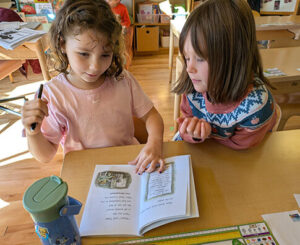 Two children reading a book together at a classroom table.