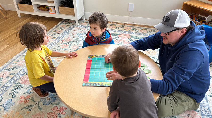 Teacher and young students playing a board game together at a classroom table.