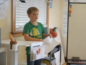 Young student presenting papers at the front of a classroom.