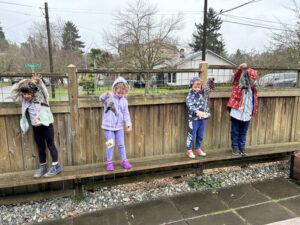 Children standing along a wooden fence during outdoor play.