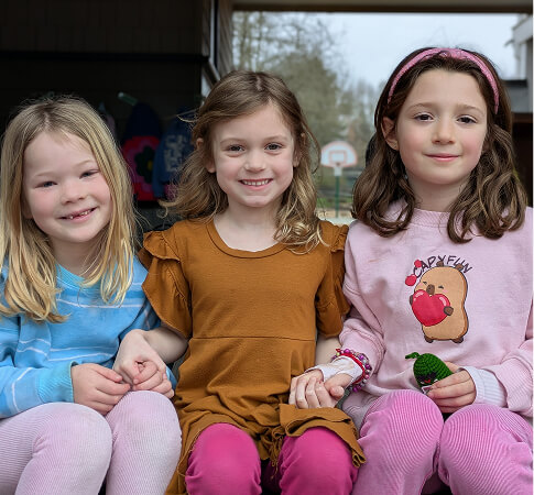 Three children sitting together outside and smiling at the camera