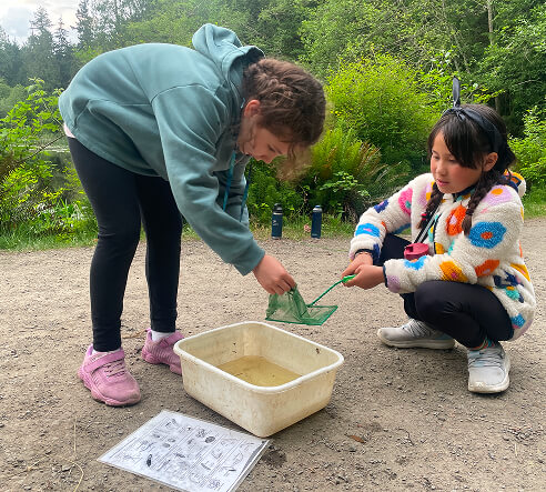 Two students collecting samples outdoors during a hands-on nature activity.