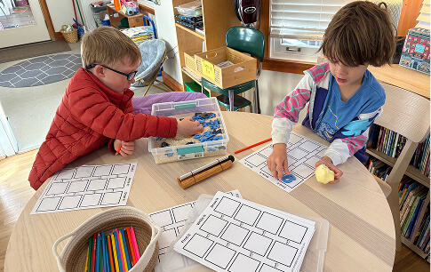 kindergarten-2 Two children working on classroom activity sheets at a table.