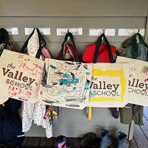 Decorated Valley School tote bags hanging above children’s backpacks and coats.